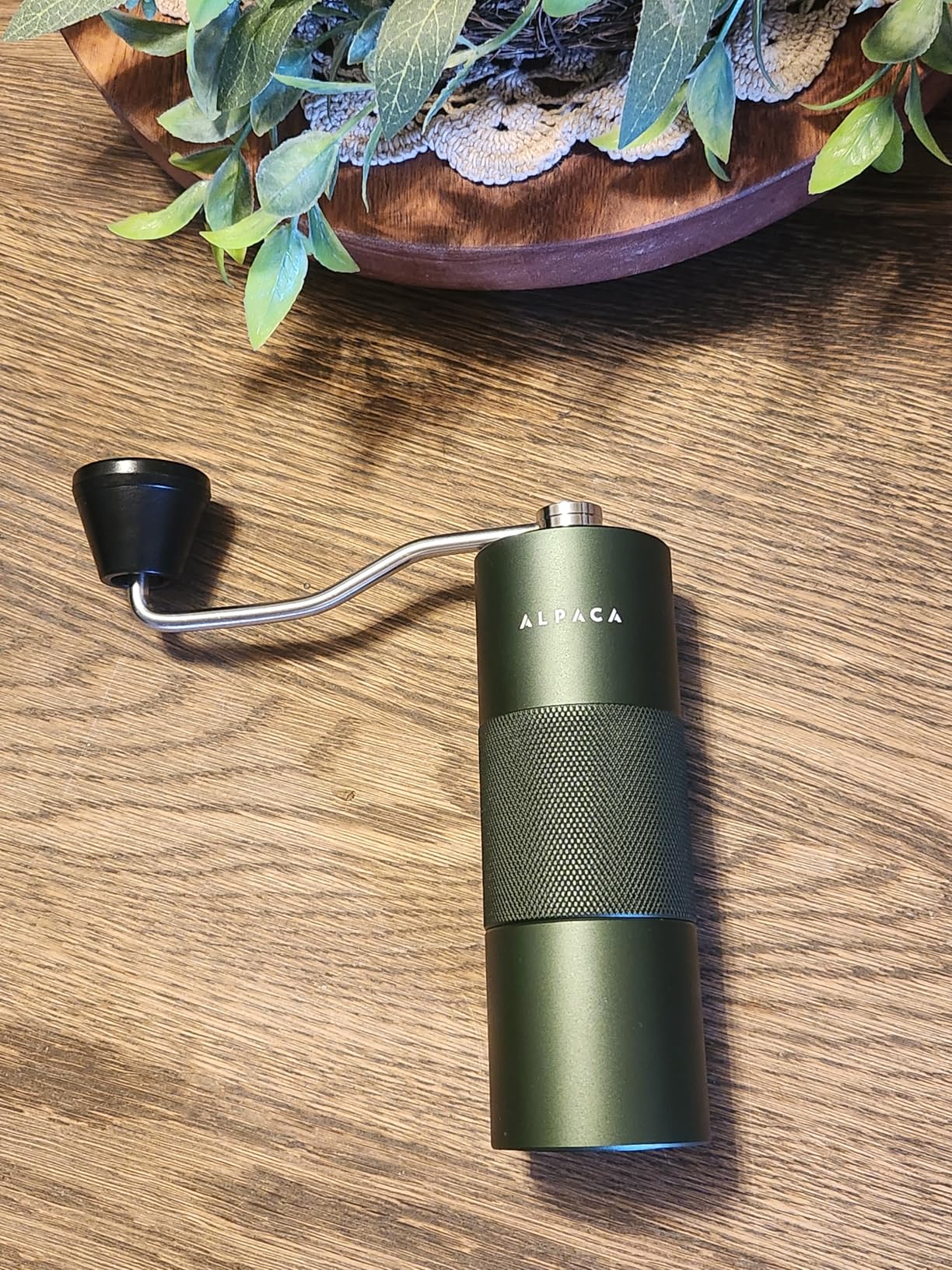 Green Alpaca hand grinder lying on a wooden table
