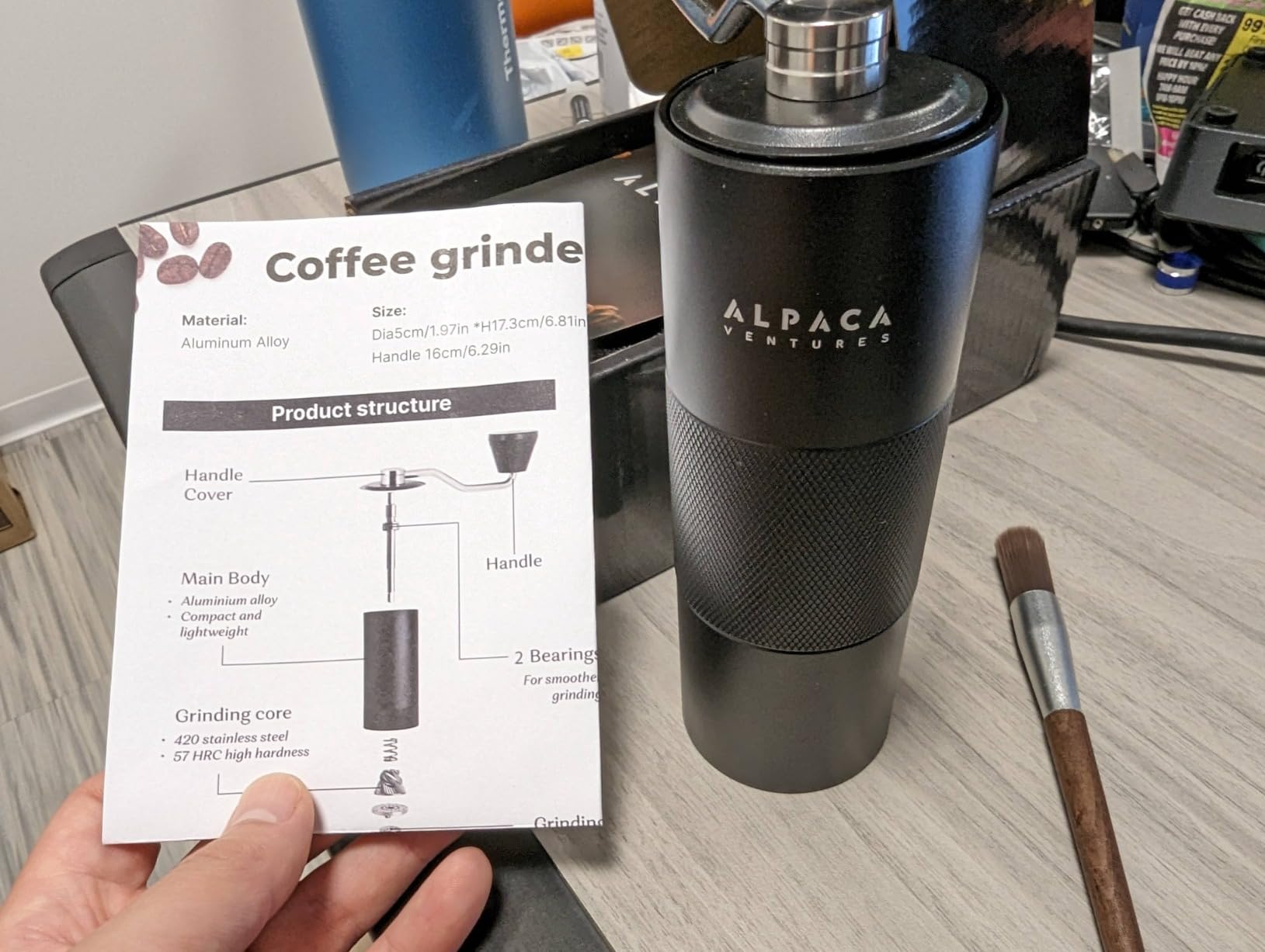 Customer holding the Alpaca product card next to the black grinder and brush on a desk
