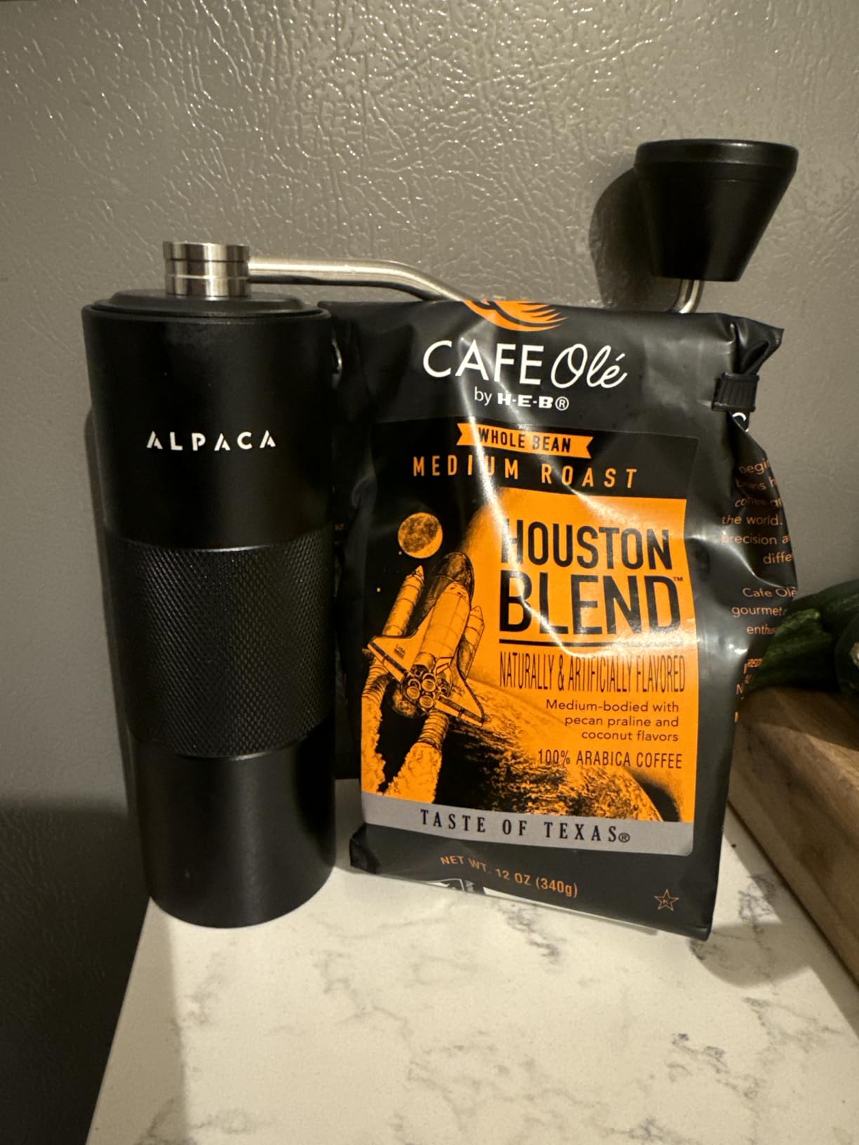 Black Alpaca grinder standing next to a bag of medium roast coffee beans